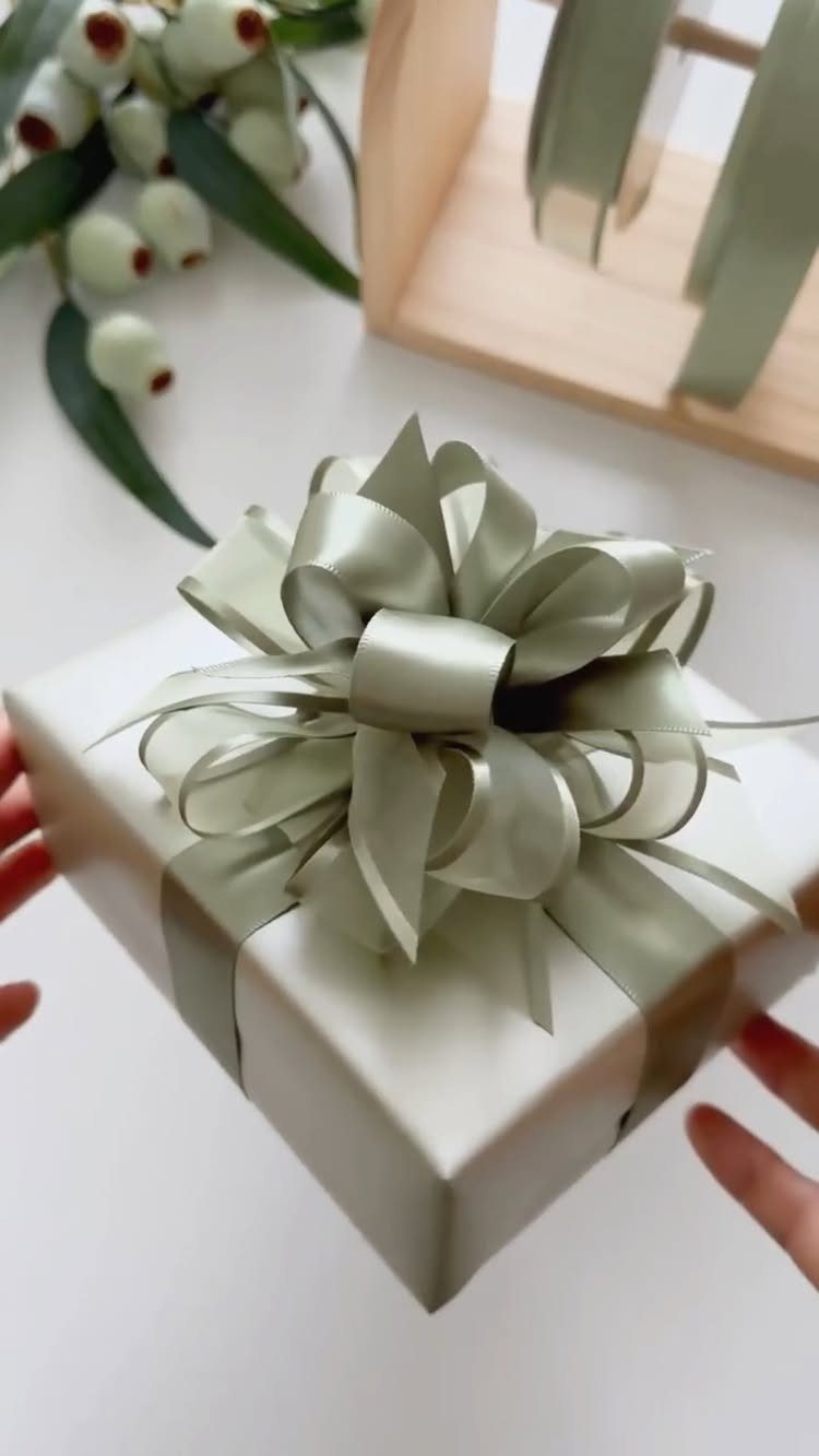 White wrapped gift with a large sage green satin bow held by hands