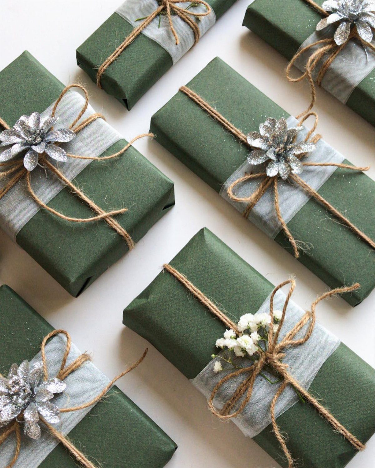 Dark green wrapped gifts tied with brown twine and silver glittery flowers.
