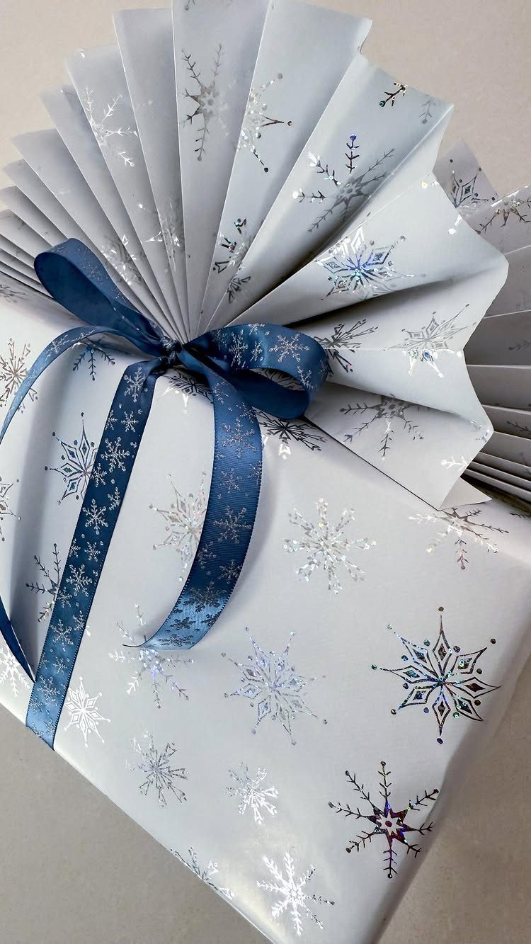 White snowflake wrapped gift with a navy blue ribbon and pleated paper topper.