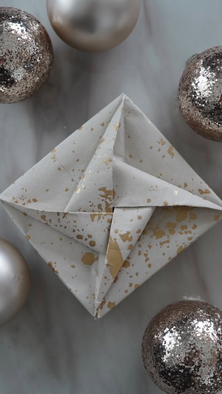 Geometric star-shaped gift wrapped in white and gold splattered paper with silver ornaments.