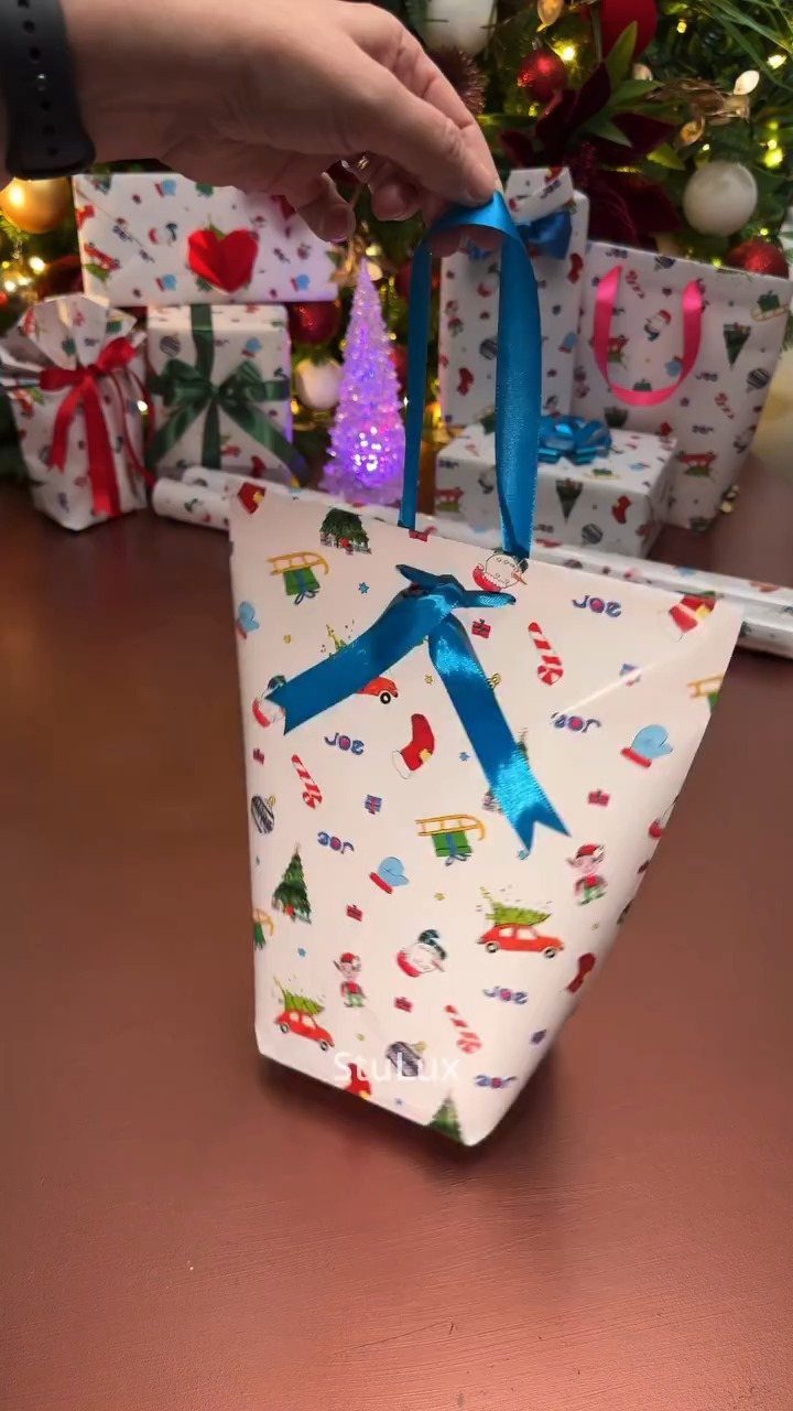 Small white Christmas gift bag with blue ribbon and festive holiday illustrations.