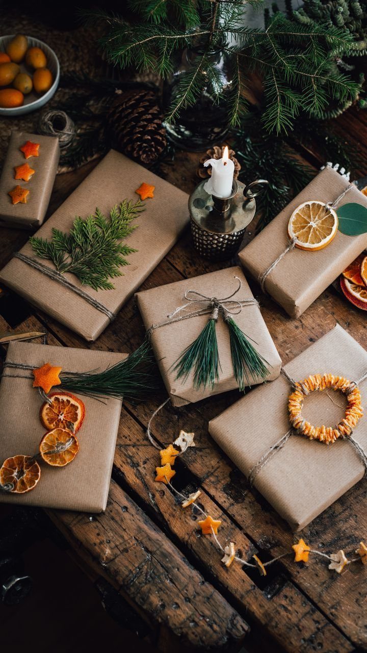 Brown paper wrapped gifts decorated with dried oranges and evergreen sprigs on wood.