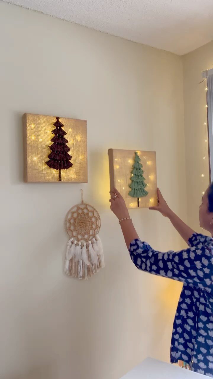 Person hanging a canvas with a green Christmas tree and fairy lights on wall