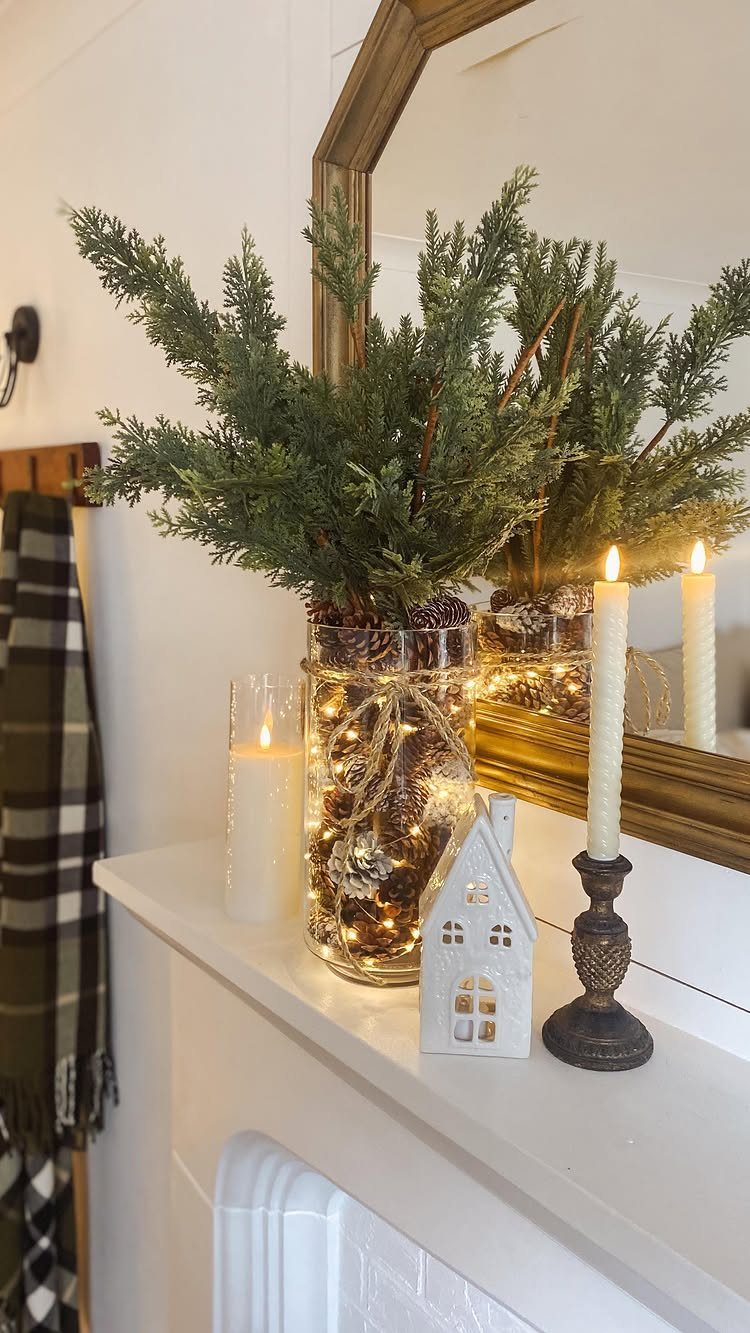 Evergreen branches in a lit glass vase on a white mantel with candles.