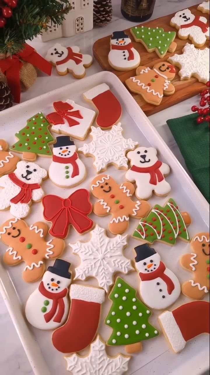 Decorated Christmas sugar cookies in festive shapes on a white tray and wooden board.