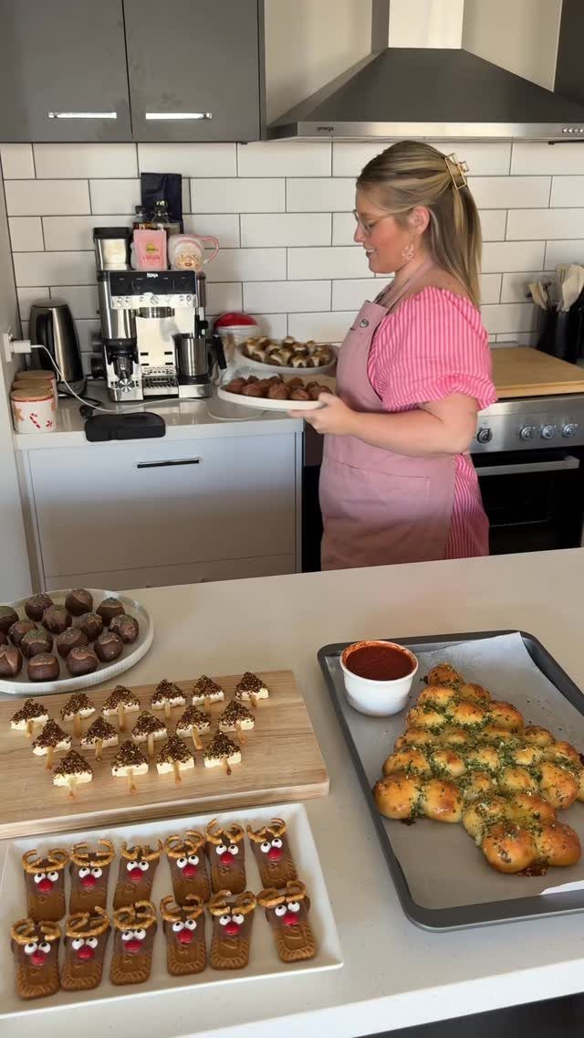 Woman in a kitchen with Christmas-themed appetizers and a tree-shaped garlic bread.