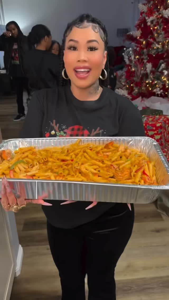 Woman holding a large tray of pasta at a Christmas party with a tree.