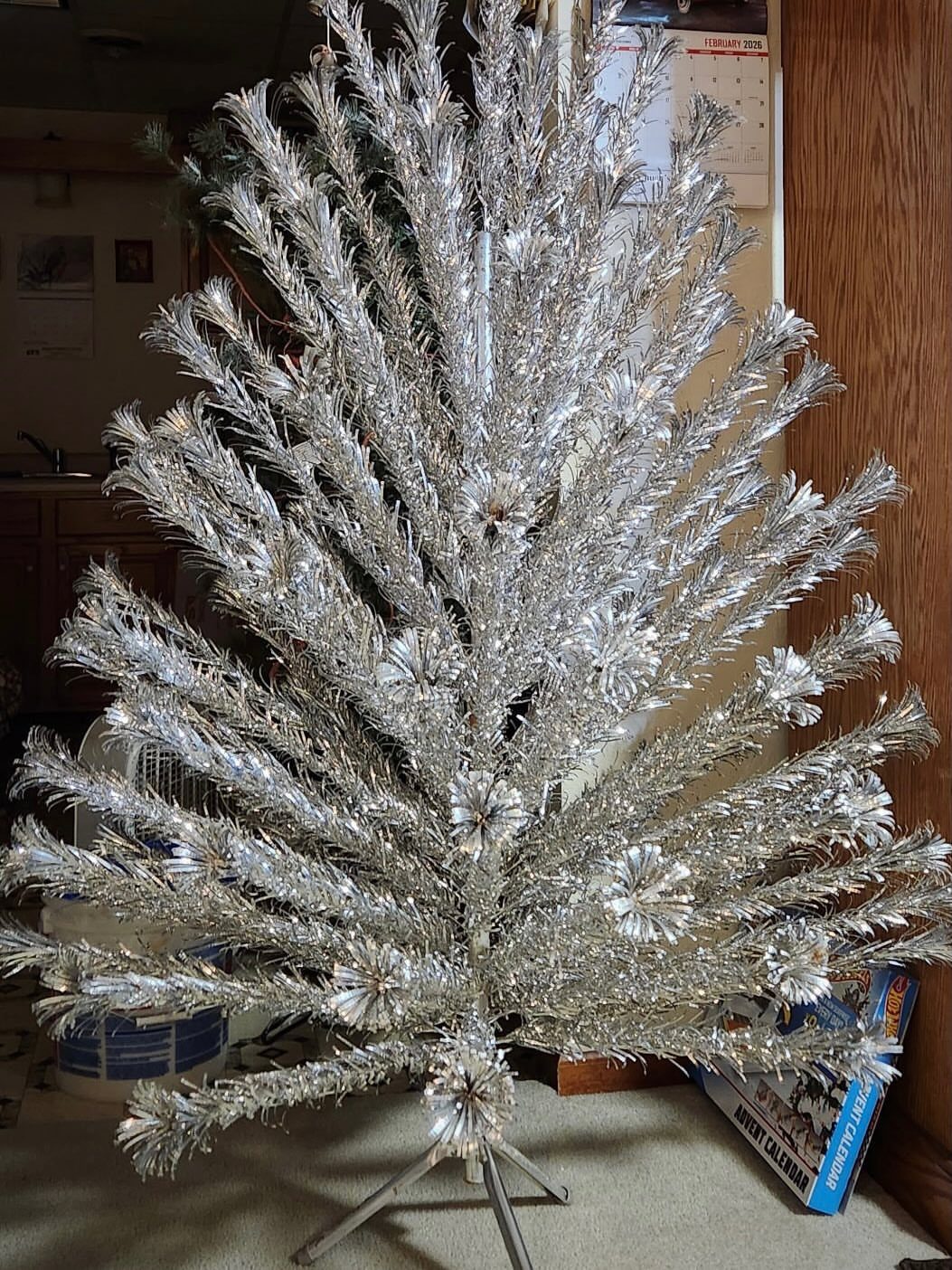 Silver tinsel Christmas tree on a metal stand against a wood paneled wall
