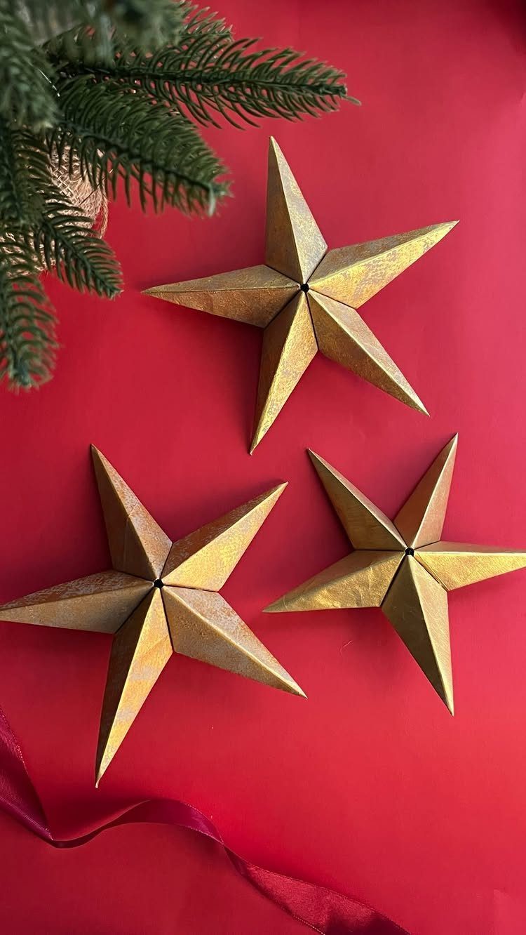 Three gold 3D paper stars on a red background with pine branches.
