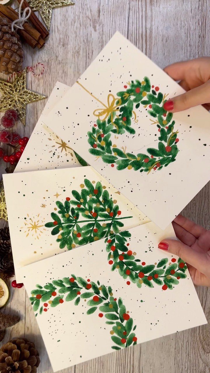 Handmade Christmas cards with painted green wreaths held over a festive wooden background.