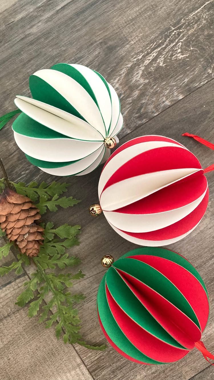 Three striped honeycomb paper ornaments with a pinecone and evergreen sprig on wood.