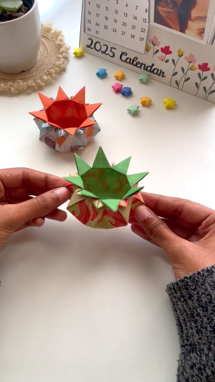 Hands holding a green and red patterned origami star bowl on white table