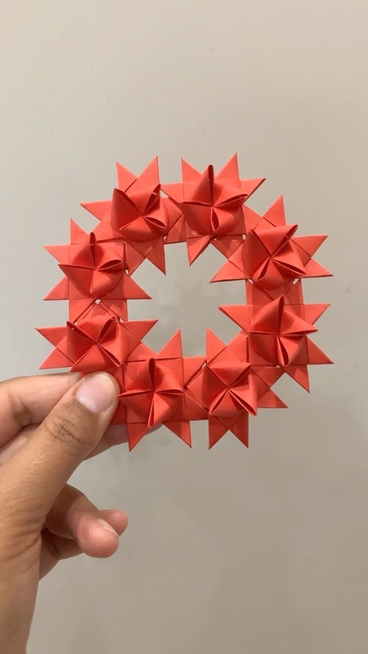 Small red paper wreath made of origami stars held by a hand.