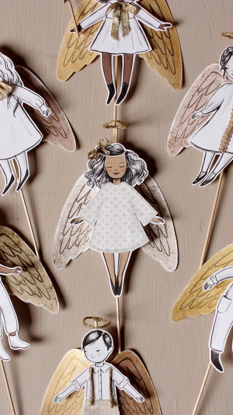 Paper angel ornaments with gold wings and white dresses on wooden sticks.