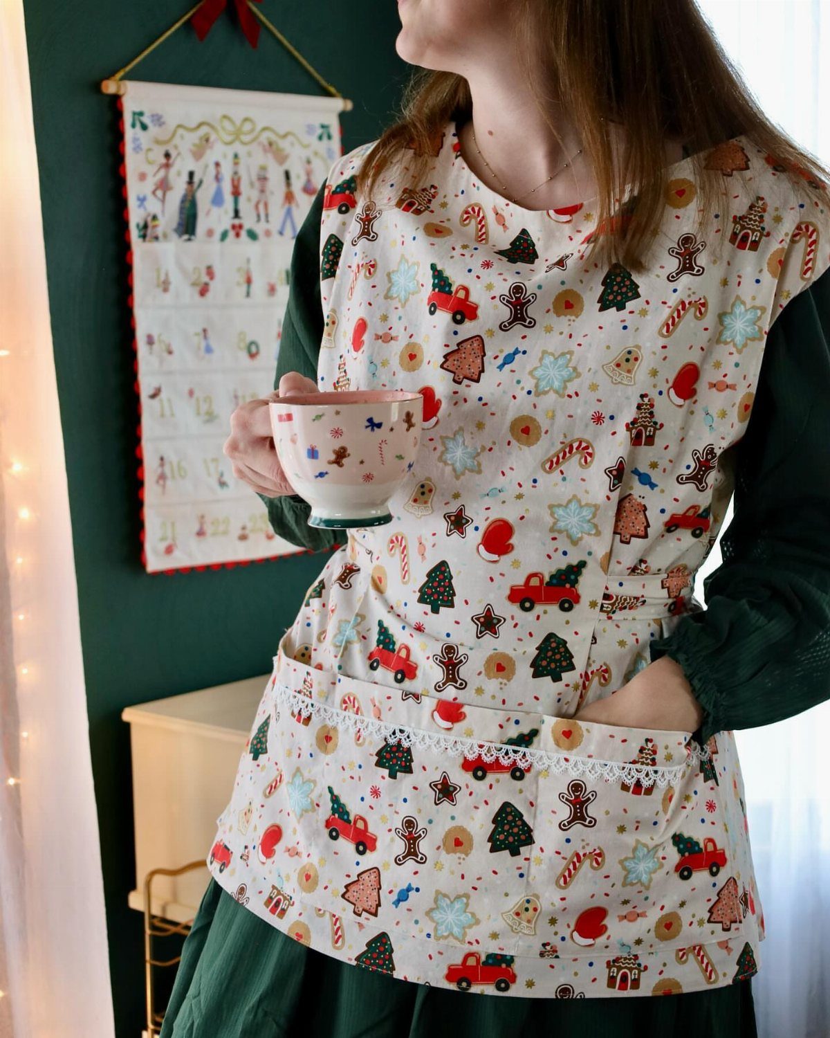 Woman wearing a white Christmas-themed apron with festive prints holding a teacup.