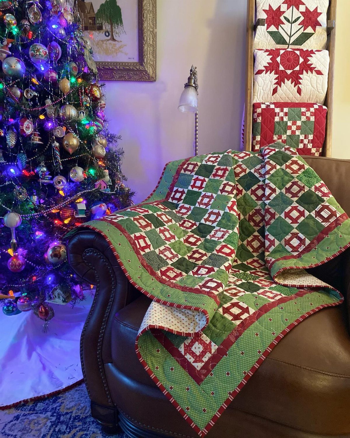 Red and green patchwork quilt draped over a brown leather armchair by a Christmas tree