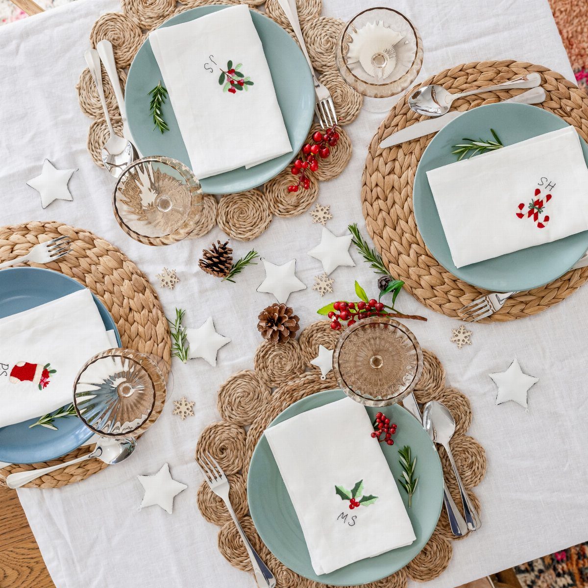 White embroidered Christmas napkins on blue plates with woven placemats and festive decorations.