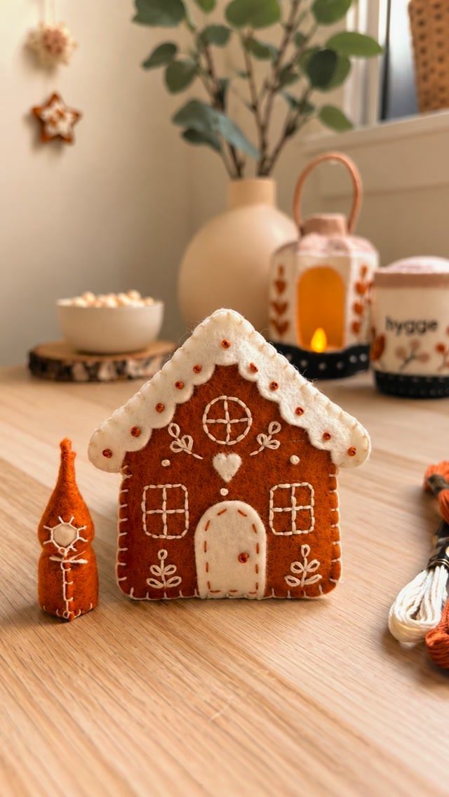 Felt gingerbread house with white stitching on a light wooden table.