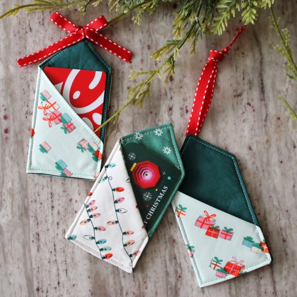 Three house-shaped fabric gift card holders with red ribbons on a wooden surface.