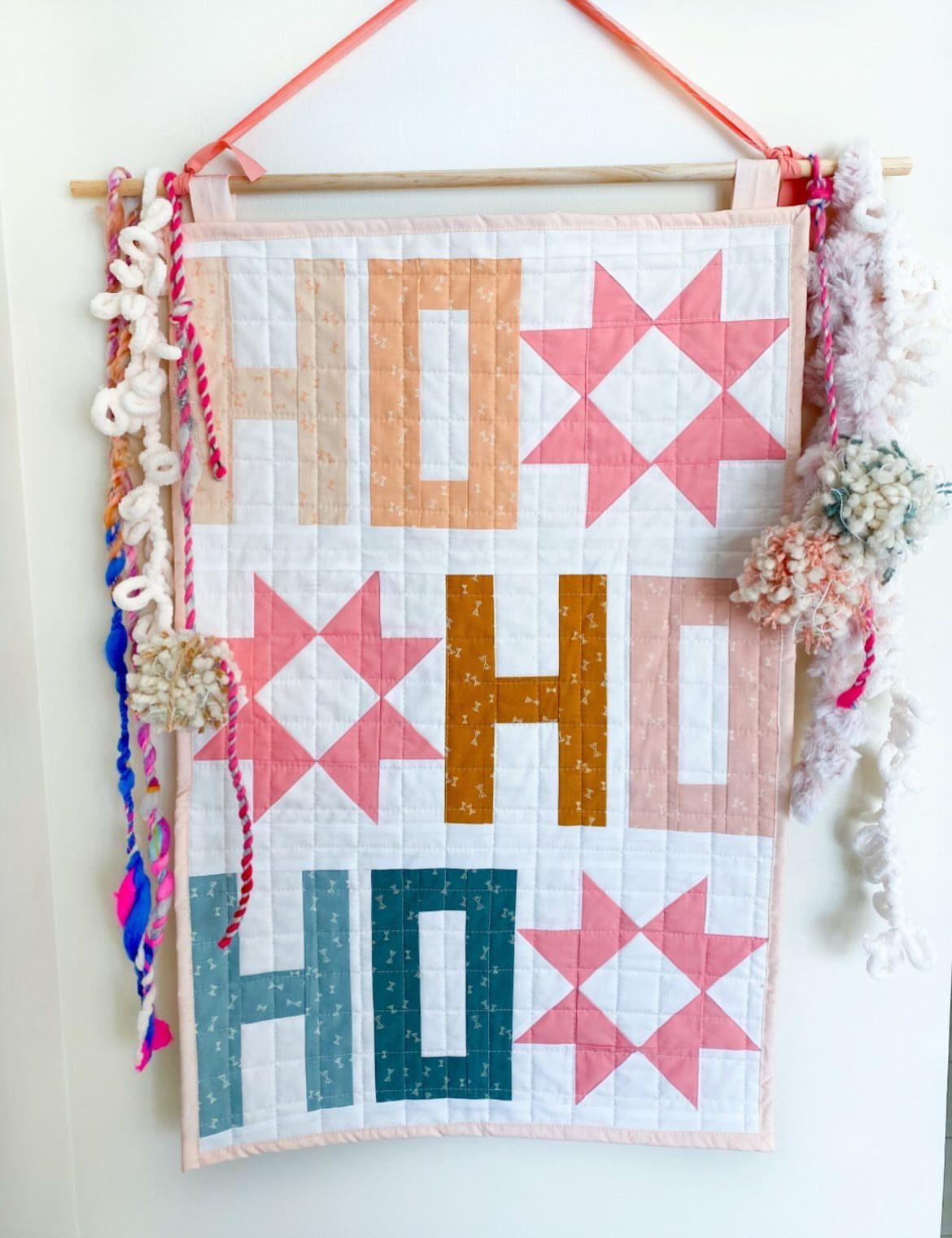 Quilted wall hanging with HO HO HO text and pink stars with colorful tassels