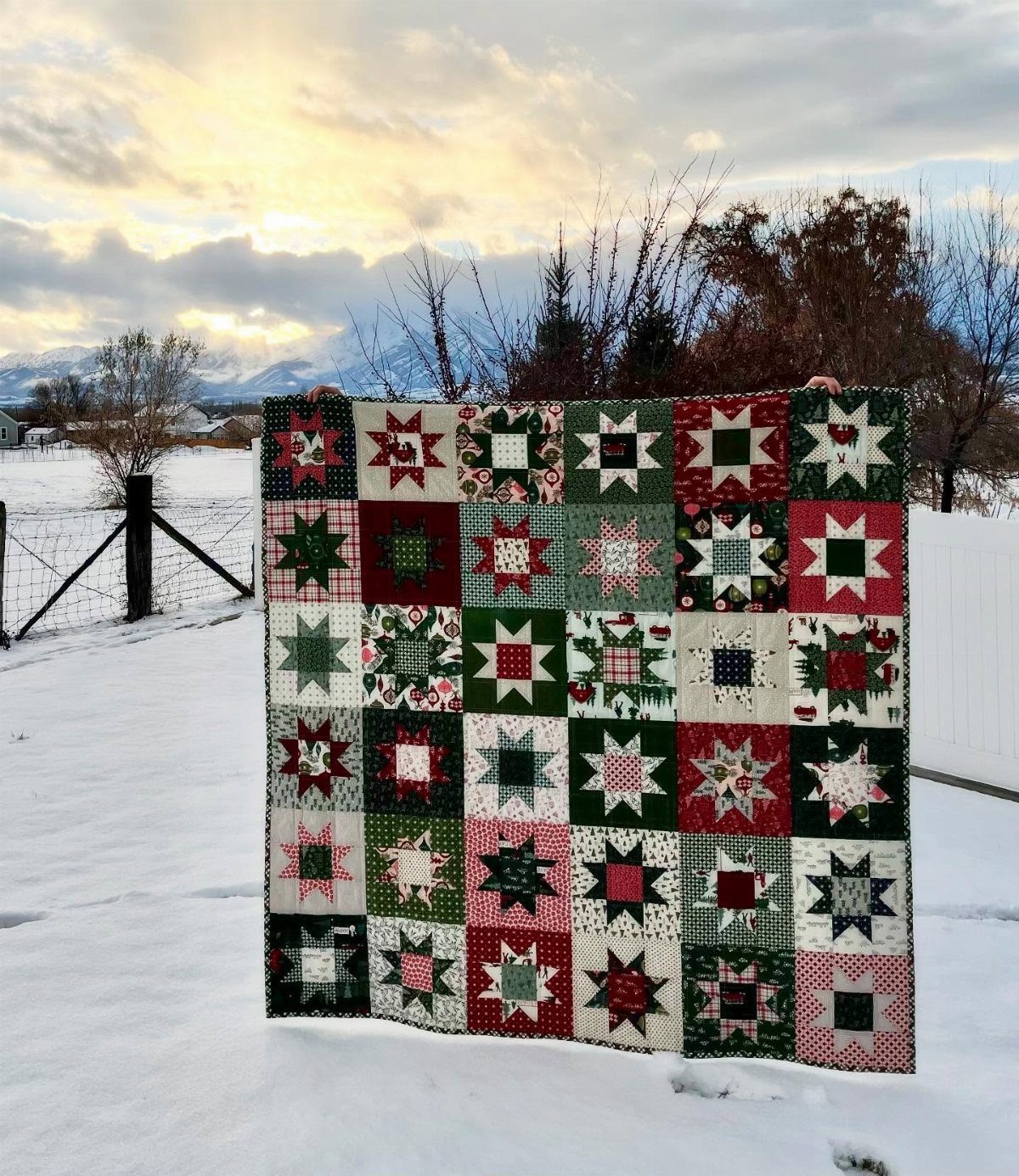 Patchwork star quilt in red and green held up in a snowy field.