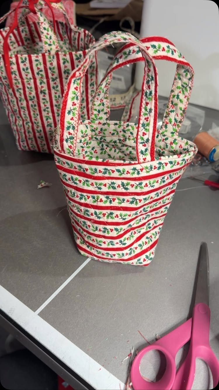 Two red and white striped fabric gift bags with holly patterns and handles.