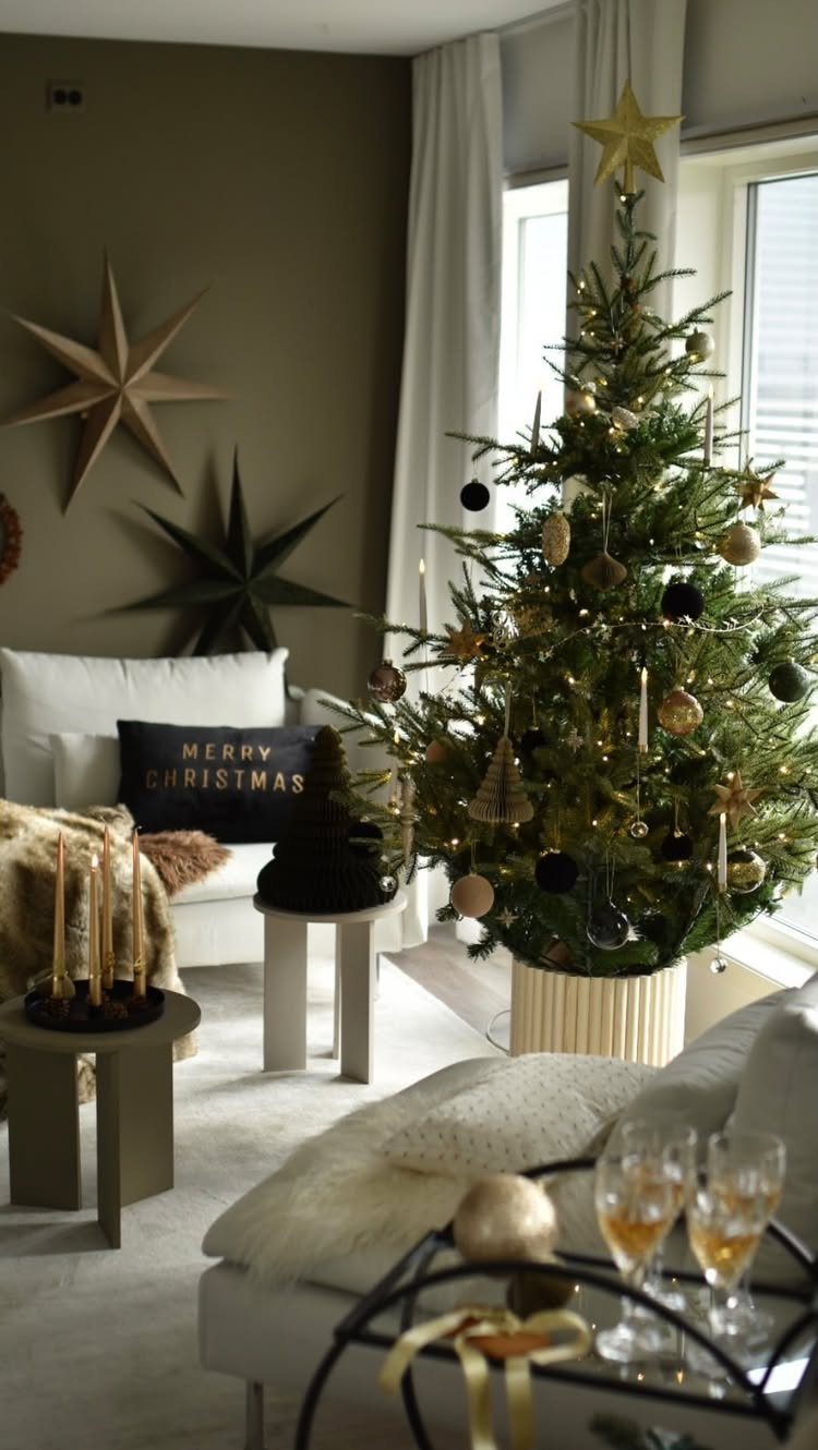 Decorated Christmas tree in a white ribbed cylindrical planter stand in a living room.