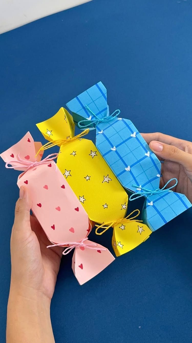 Three candy-shaped wrapped gifts in pink, yellow, and blue held by hands.