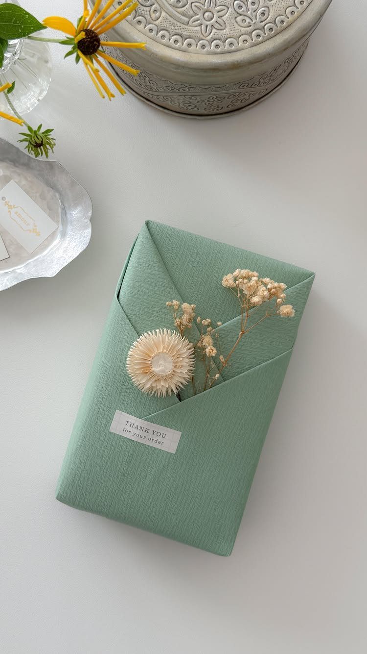 Green wrapped gift with a dried flower sprig and small thank you tag.
