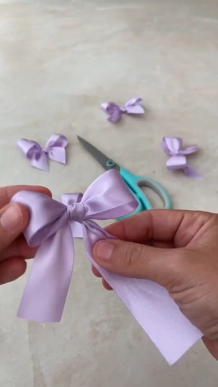 Hands holding a light purple satin bow next to scissors and other bows.