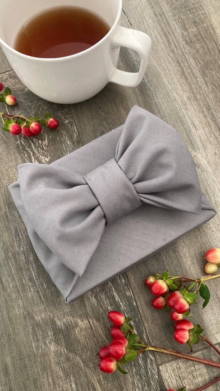 Grey fabric wrapped gift tied in a bow next to tea and berries