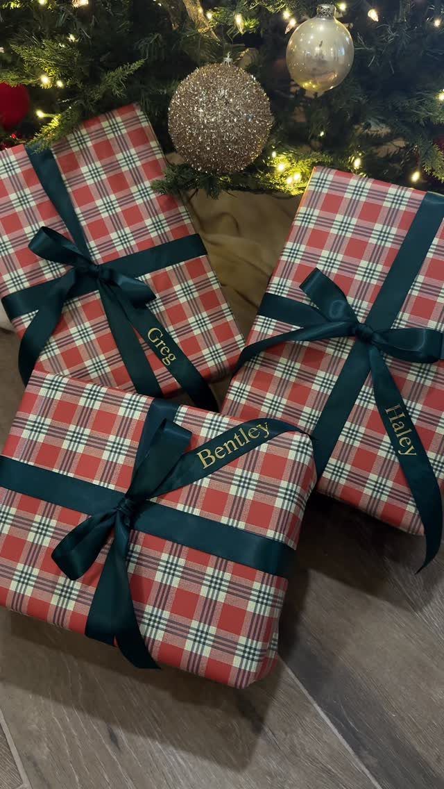 Plaid wrapped Christmas gifts with green ribbons and gold name tags under a tree