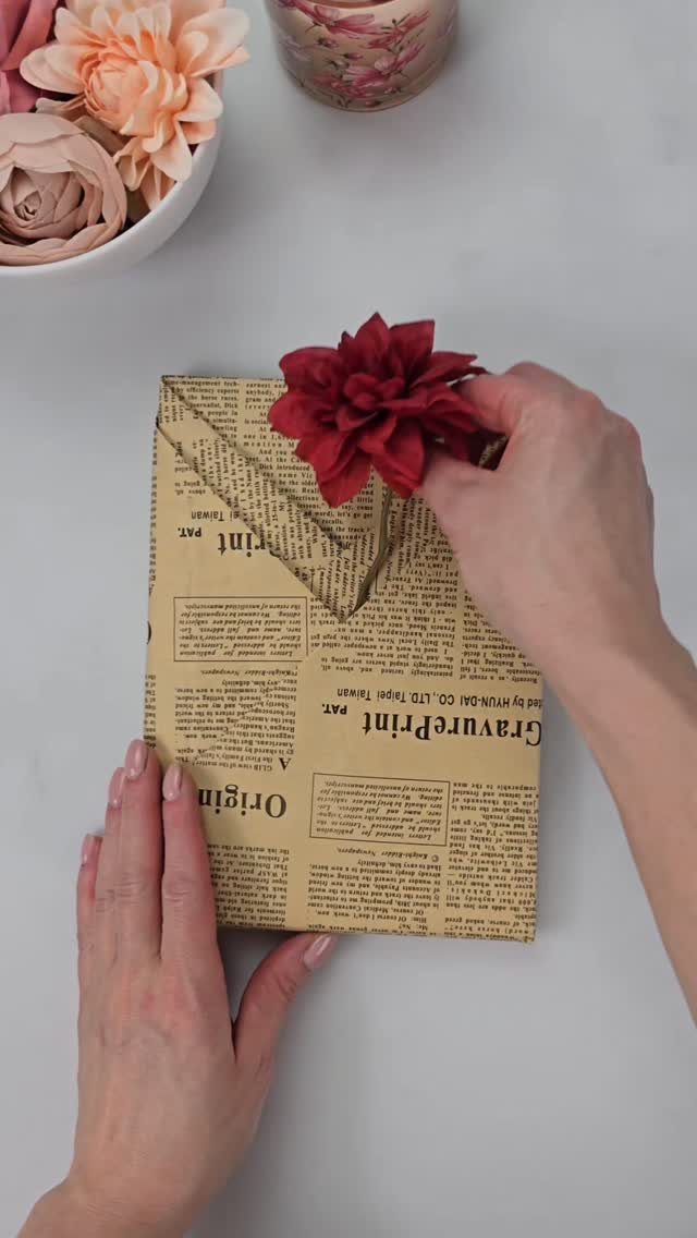 Gift wrapped in vintage newsprint paper tied with twine and a red flower.