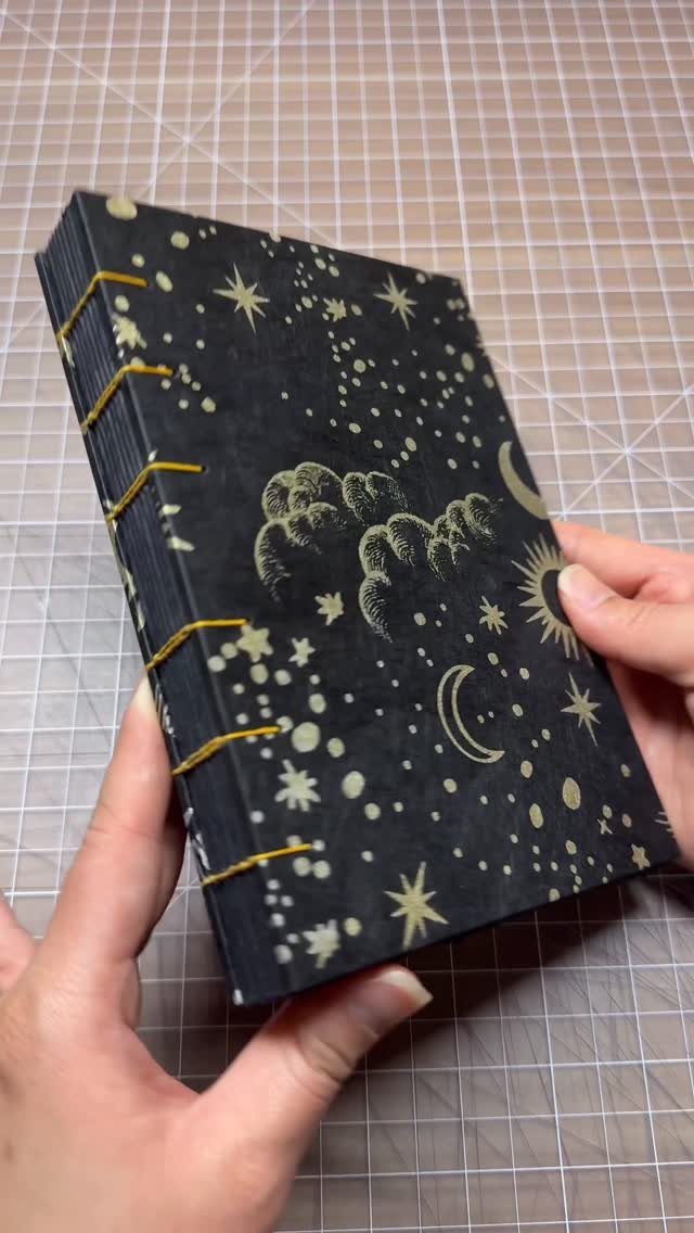 Black celestial journal with gold stars and moons held by two hands