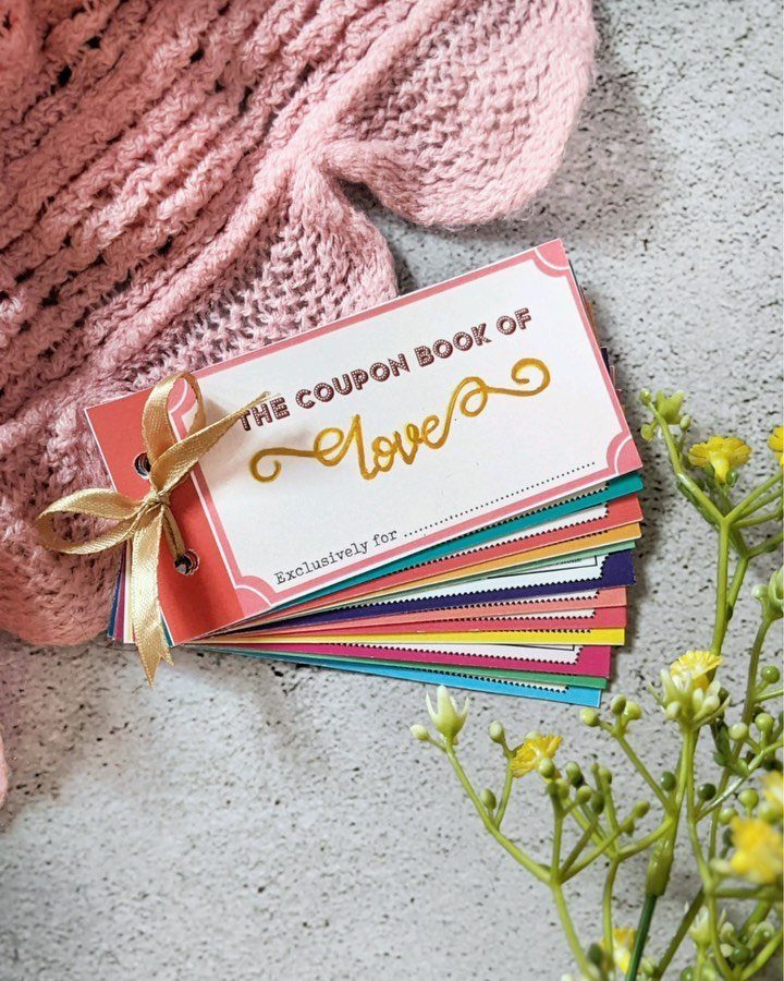 Handmade coupon book tied with gold ribbon next to pink knit and yellow flowers