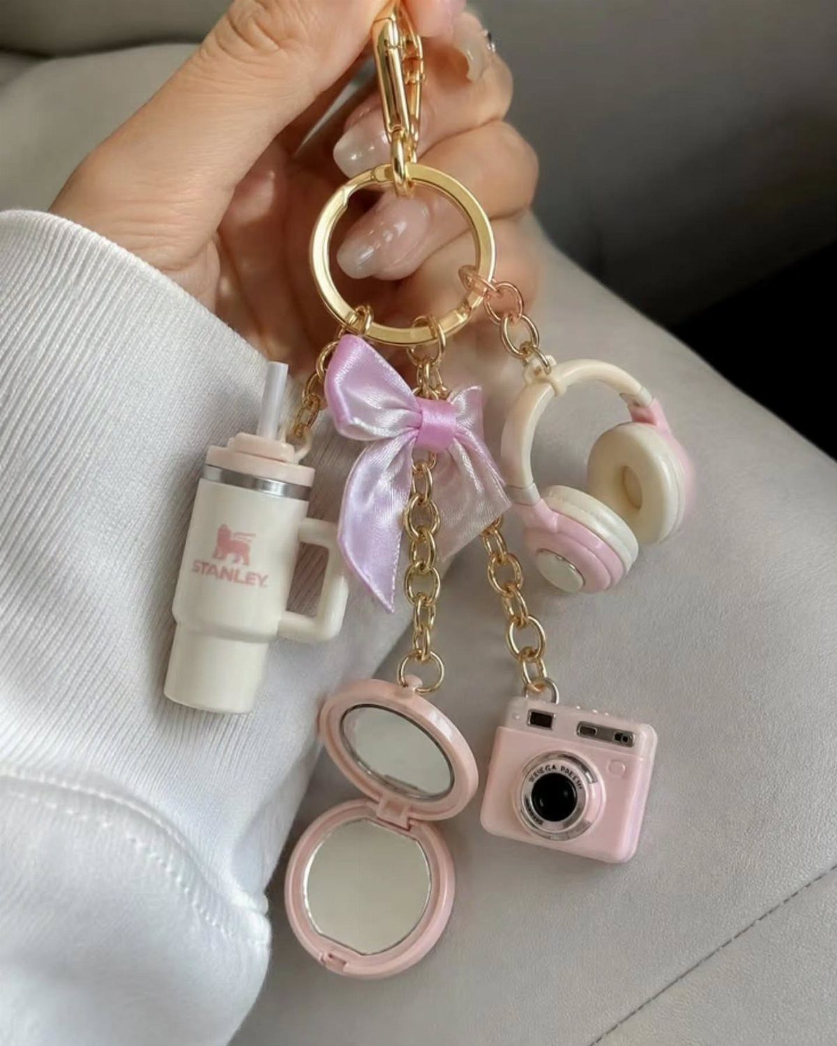 Gold keychain with miniature pink and white charms including a camera and cup.