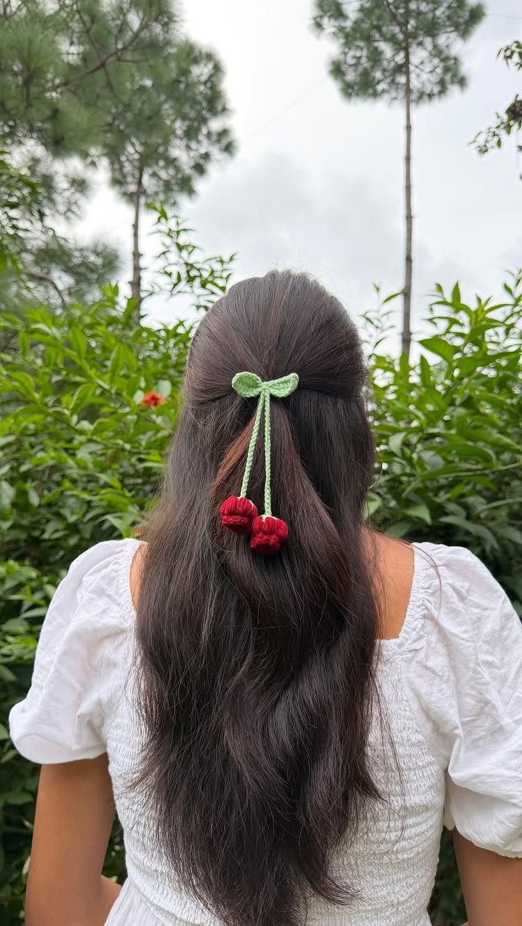 Green crocheted bow hair clip with red pom-poms in long dark hair.