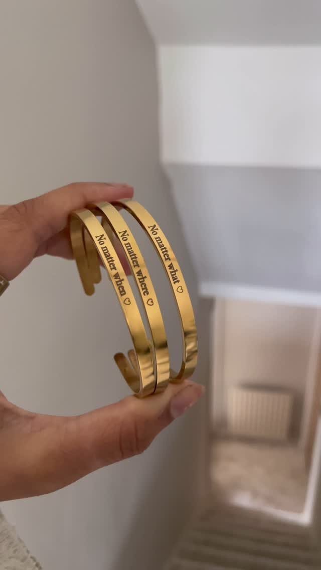 Three gold cuff bracelets with engraved friendship quotes held in a person's hand.