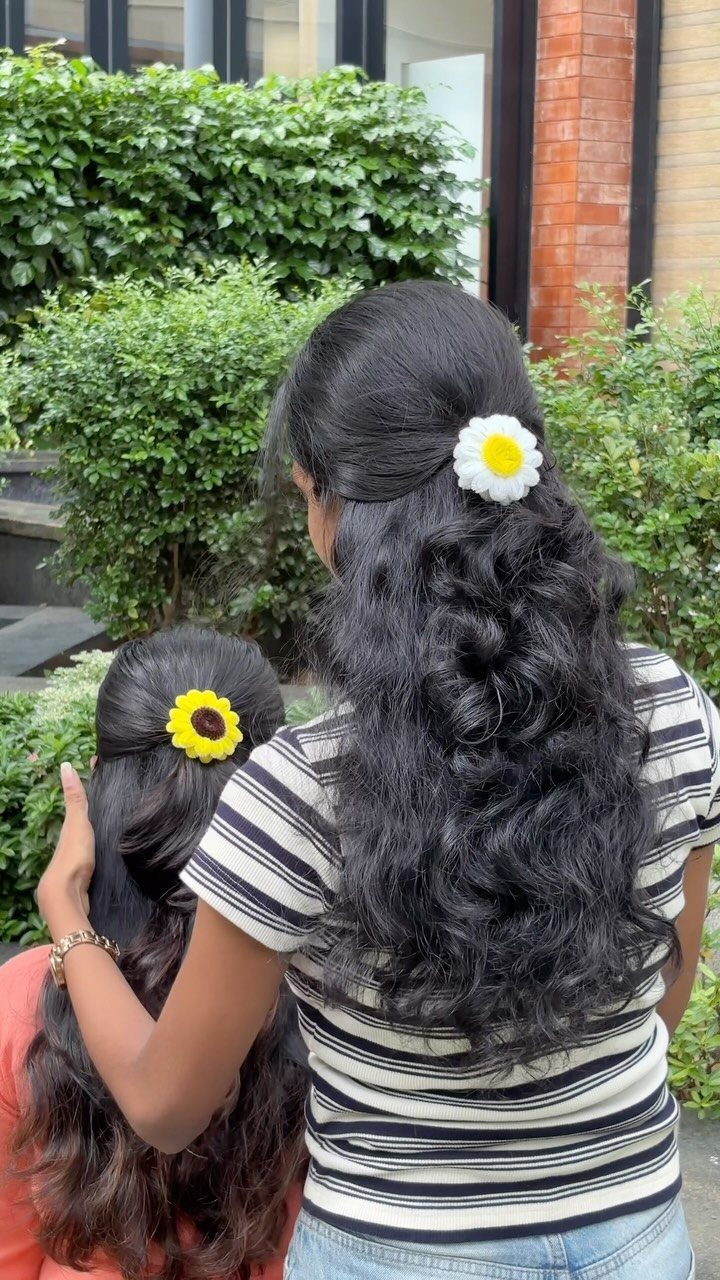 Two women with long dark hair wearing flower-shaped hair clips outdoors.