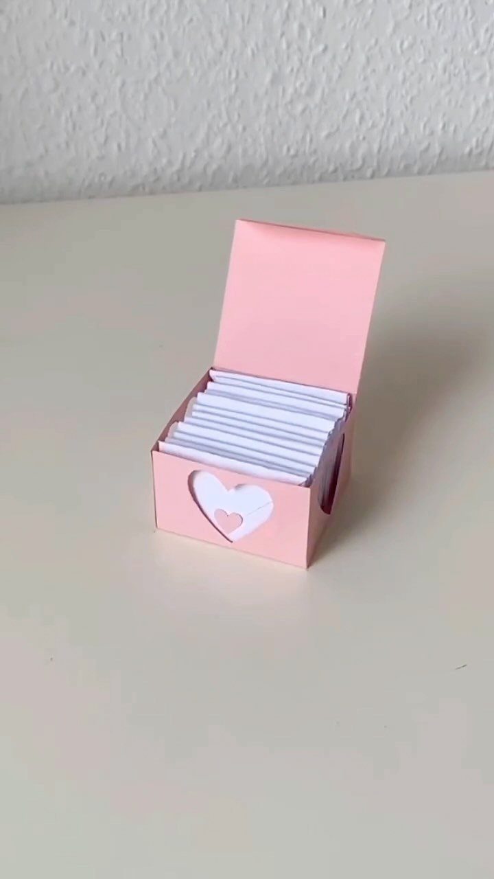 Small pink paper box with heart cutout filled with white paper slips.