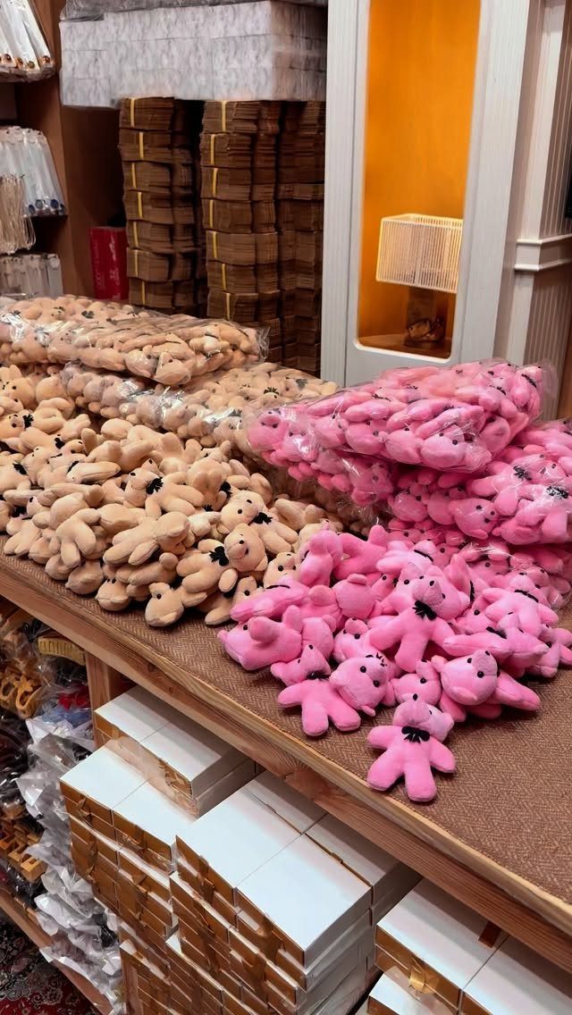 Small pink and beige plush toys piled on a wooden store shelf.
