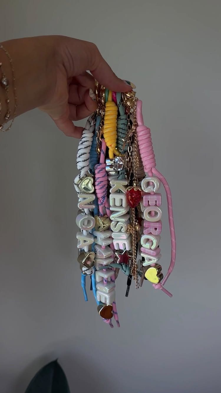 Hand holding several colorful handmade friendship bracelets with personalized name beads.
