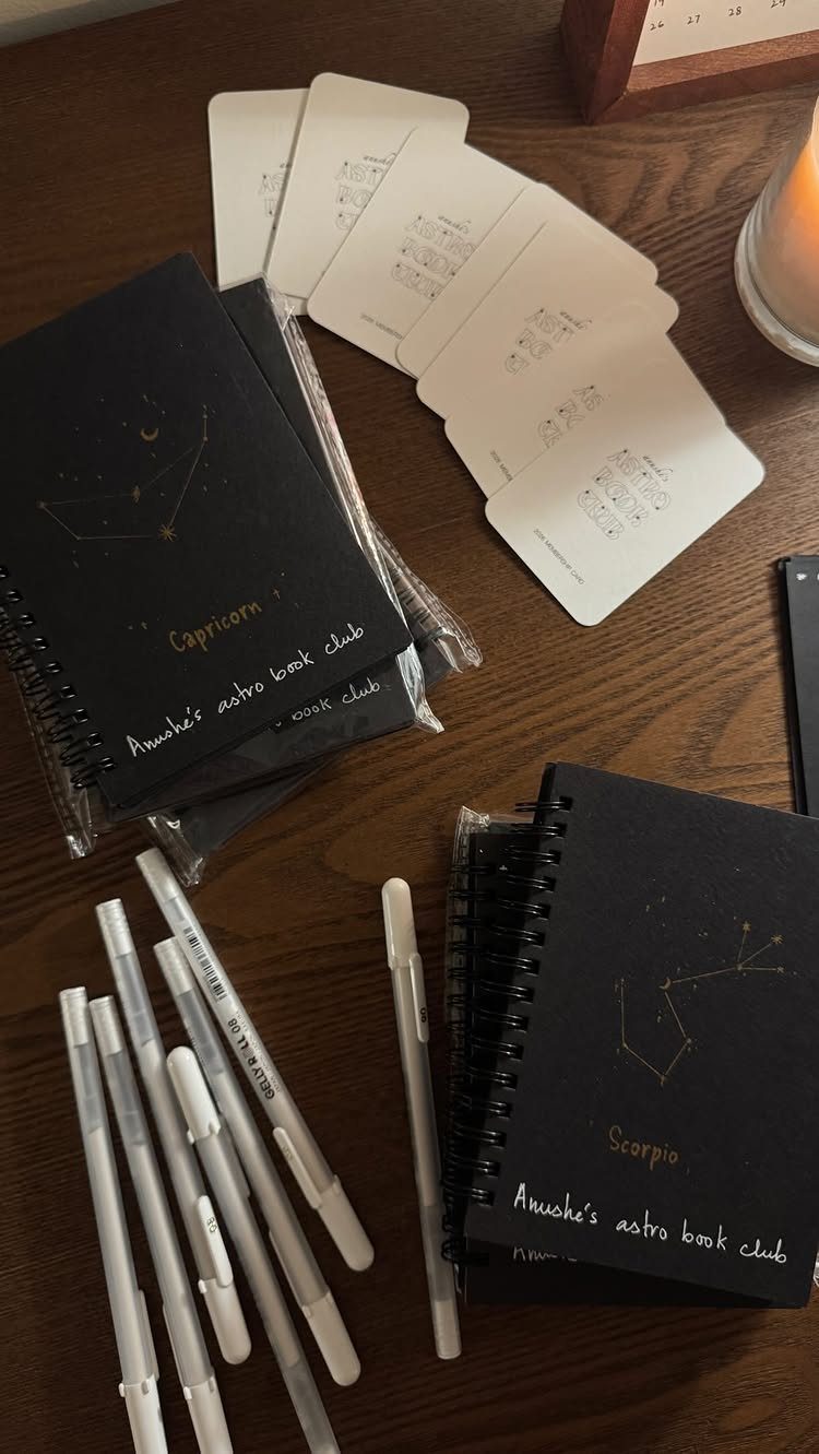 Black zodiac notebooks with gold constellations and white markers on a wooden table.