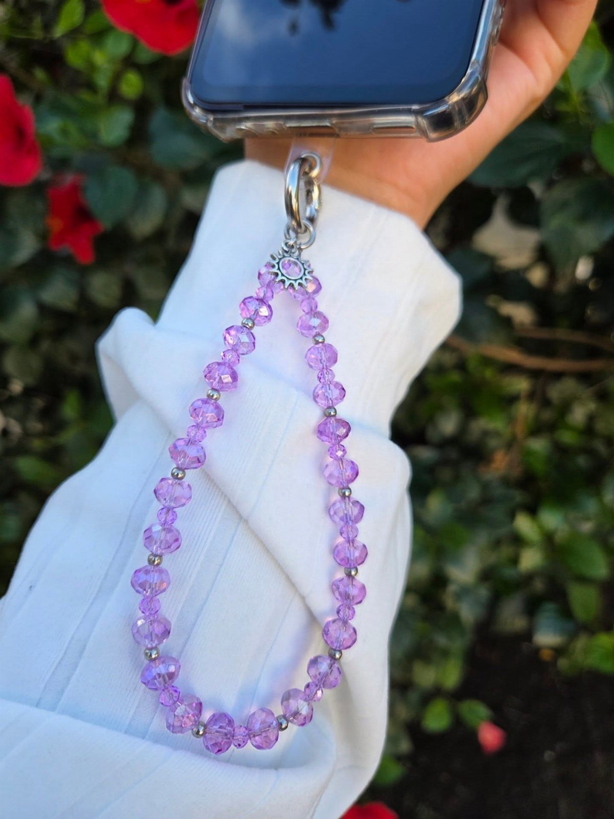 Purple beaded phone wrist strap held against a white sleeve and garden background