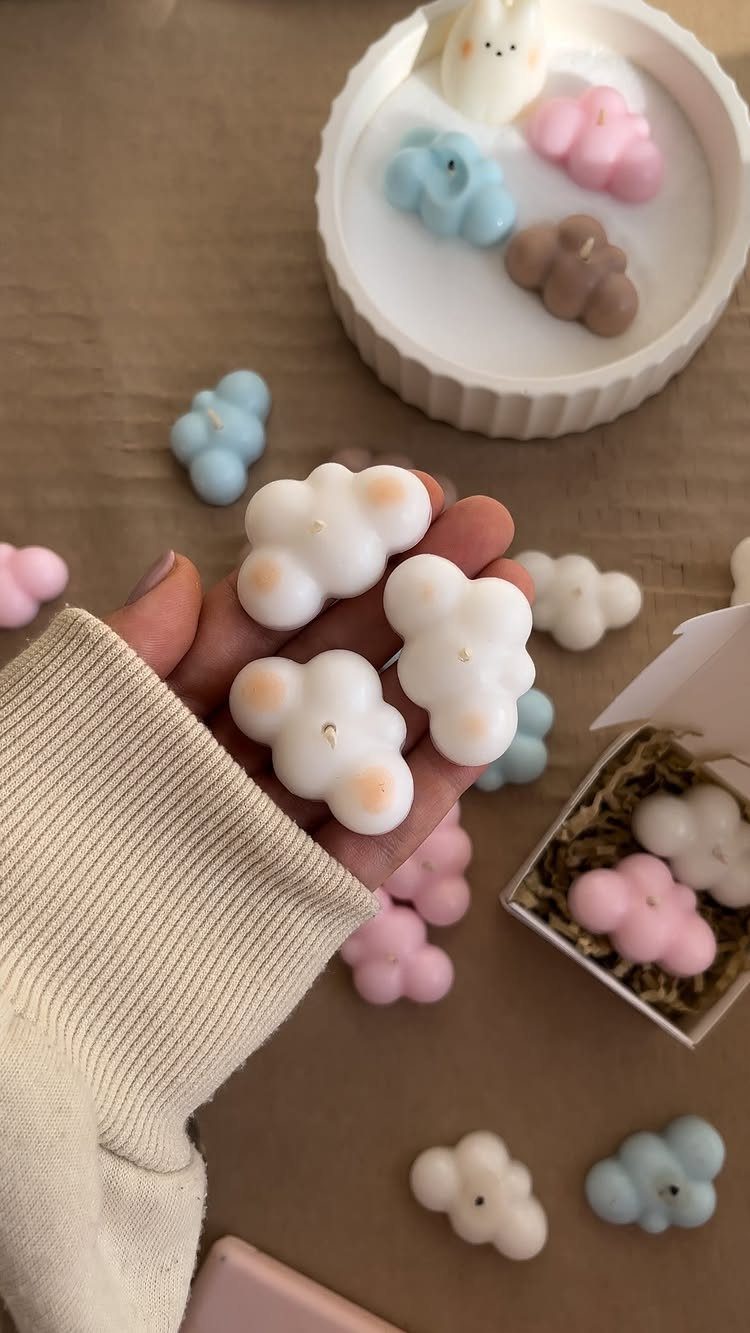 Cloud-shaped candles in pastel colors held in a hand and scattered around.
