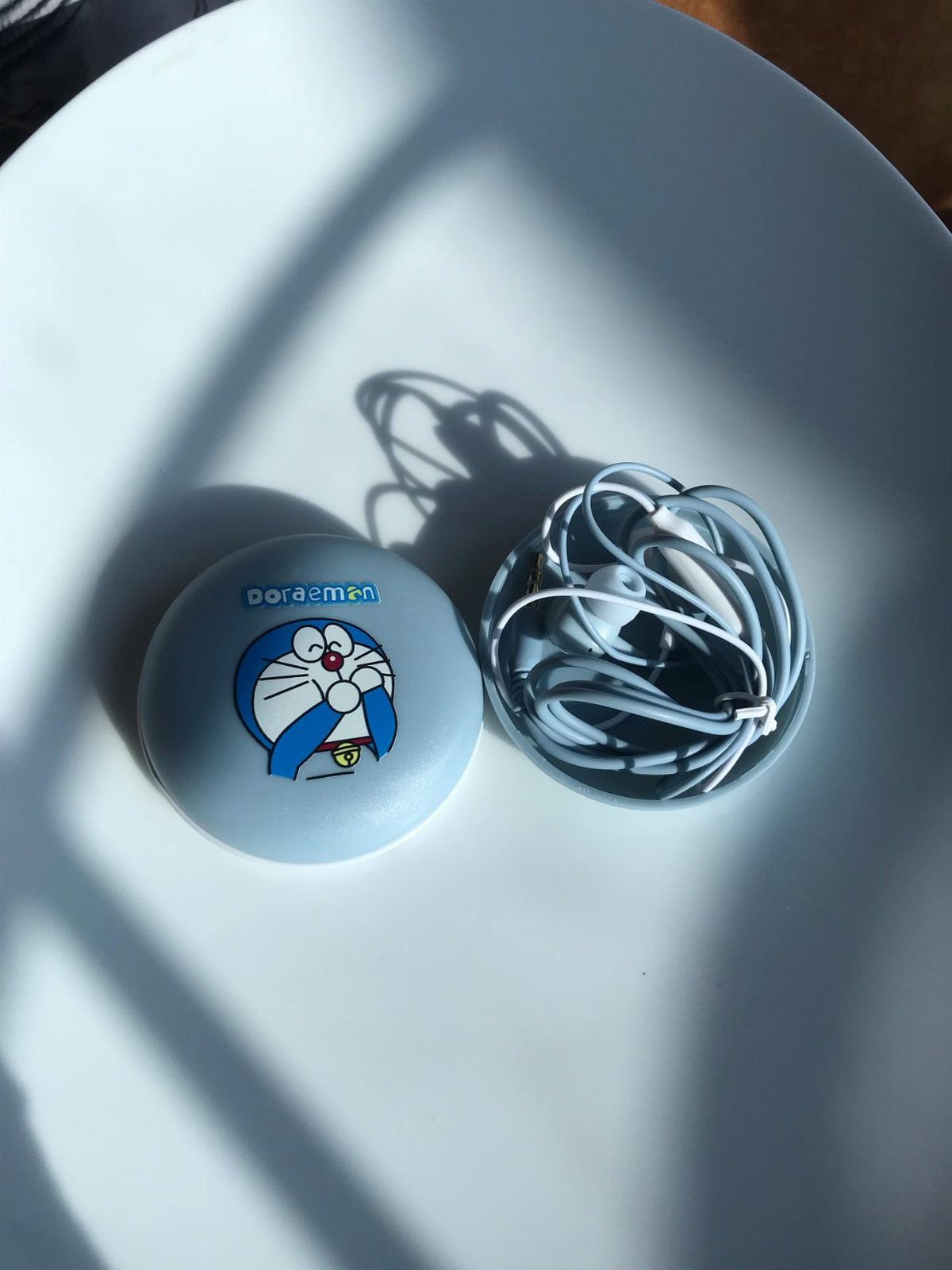 Light blue Doraemon earphone case and white wired earbuds on a white surface