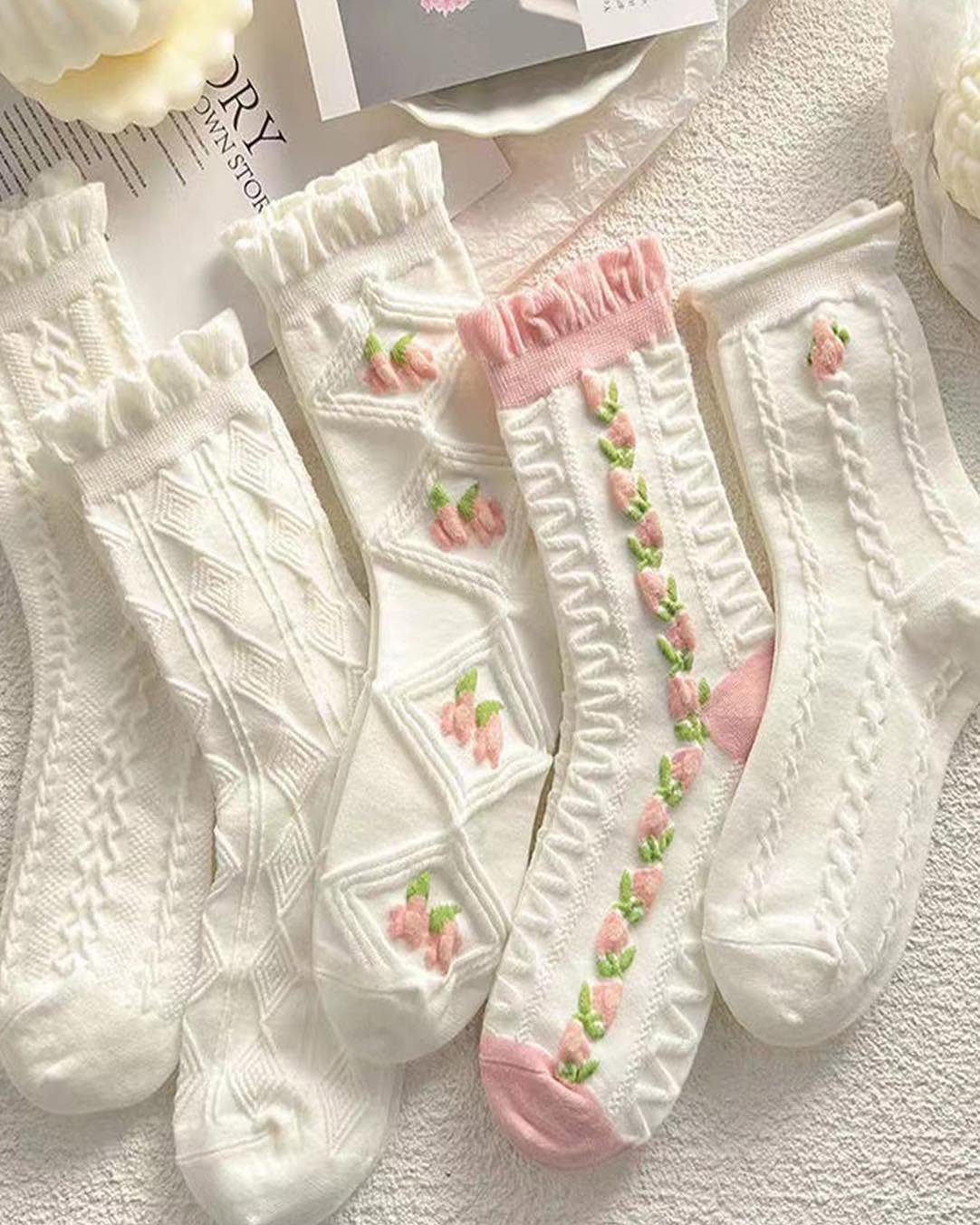 White crew socks with cable knit patterns and pink floral embroidery on white background