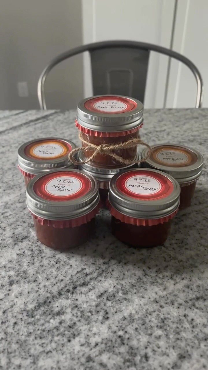 Six small jars of homemade apple butter with red labels on a countertop
