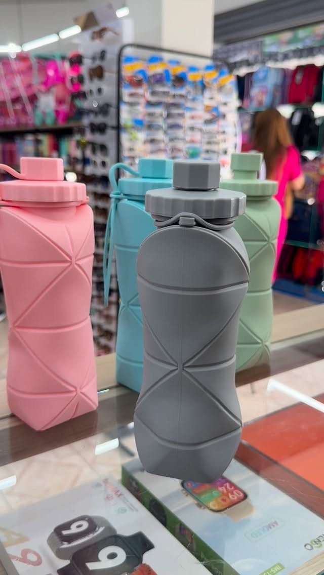 Four matte reusable water bottles in pink, blue, grey, and green on a shelf.