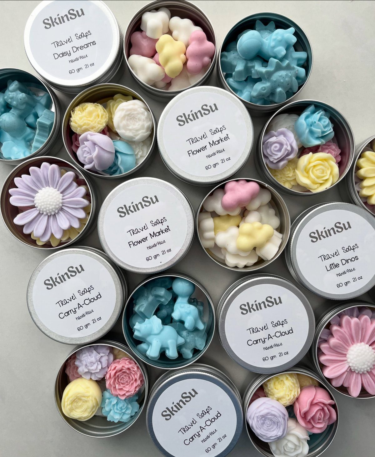 Pastel colored shaped soaps in small silver tins with white labels.